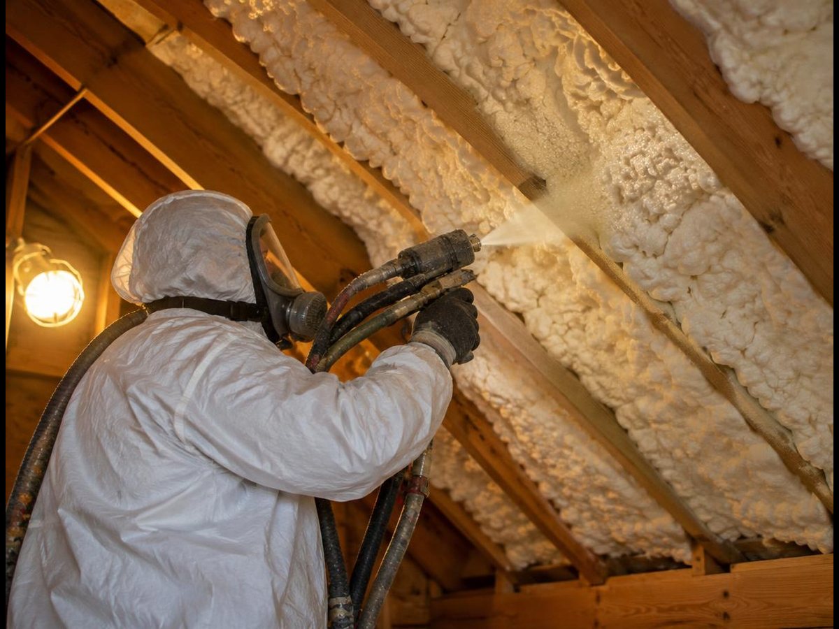 Insulation installer spraying foam insulation between rafters in an American attic